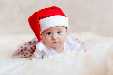 European six-month-old baby girl with big beautiful eyes in red santa cap lies on her stomach for Christmas. Photo shoot babies