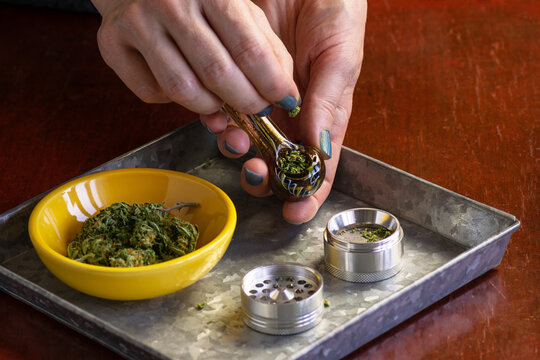 Woman's Hands Filling Glass Pipe with Medical Marijuana or Hemp Flowers Over Tray with Smoking Accessories