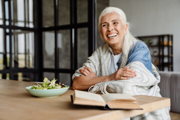 Smiling senior woman reading a book - obrazy, fototapety, plakaty