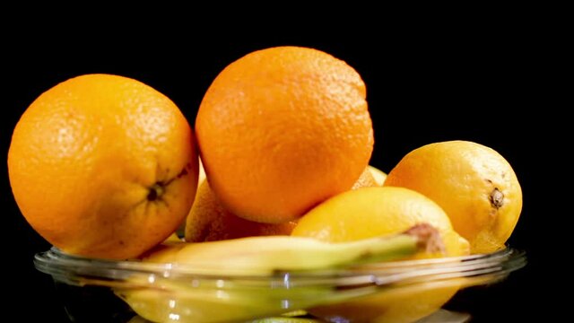 Fresh Tropical Fruit on Plate, Orange, Lemon, Banana. Spinning Close Up Isolated on Black Background, Full Frame