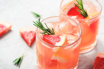 Refreshing grapefruit cocktail with ice and rosemary on a grey background.