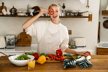 Beautiful happy woman making fun with vegetables while cooking lunch