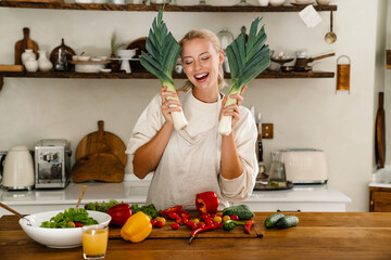Beautiful cheerful woman making fun with leeks while cooking lunch