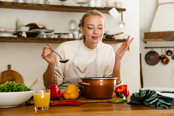 Beautiful pleased woman cooking soup and smiling while making lunch