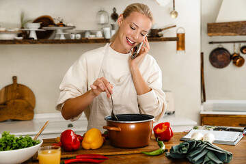 Beautiful woman smiling and talking on cellphone while making lunch