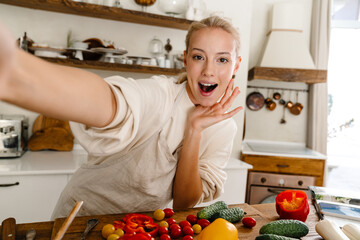 Astonished woman taking selfie and expressing surprise while making lunch
