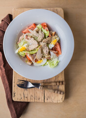 Lettuce and croutons topped with shredded cheese, Cezar salad on white plate over wooden table