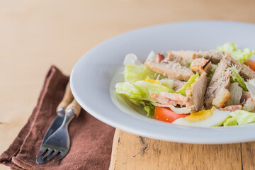 Lettuce and croutons topped with shredded cheese, Cezar salad on white plate over wooden table