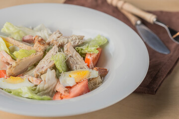 Lettuce and croutons topped with shredded cheese, Cezar salad on white plate over wooden table