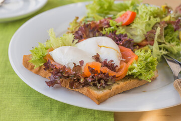 Plate with pashot eggs served on bread with salmon and vegetables