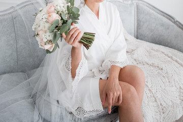 the bride in a white robe in the morning holds a bouquet in her hands