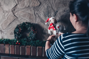 Woman decorating and preparing her home for christmas. Woman decorating the fireplace with gifts, and christmas decoration such as garland, lights and christmas wreath.