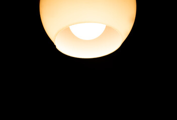 Bright dusty yellow light bulb / lamp with white glass shade in the dark room
