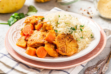 Chicken stew with pumpkin, carrots, tomatoes, spices and garlic, served with couscous on a ceramic plate. Moroccan food, Maghreb cuisine. Chicken with vegetables and couscous close-up.