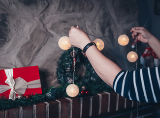 Woman decorating and preparing her home for christmas. Woman decorating the fireplace with gifts, and christmas decoration such as garland, lights and christmas wreath.