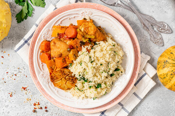 Chicken stew with pumpkin, carrots, tomatoes, spices and garlic, served with couscous on a ceramic plate. Moroccan food, Maghreb cuisine. Chicken with vegetables and couscous on a gray table top view