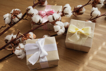 christmas gifts in craft paper, with yellow, white and pink ribbons and branches with cotton flowers on the wooden table