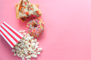Slice of cheese pizza on a plate , donuts and popcorn on pink 