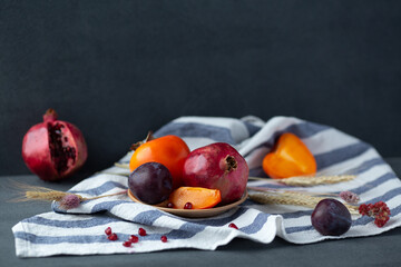 Autumn fruits still-life. Pomegranate, persimmon and plum on dark gray background.