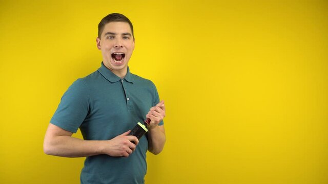 A young man inflates a long blue balloon with a pump on a yellow background. Man in a green polo.