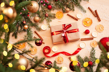 Present wrapped in parchment paper with red bow on a bright Christmas table. Decorated background with cinnamon, orange, ribbon near the Christmas tree with bright lights