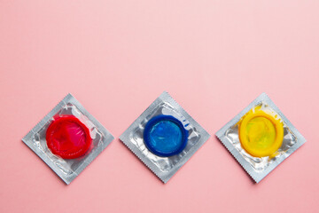 Close up shot of various colored condoms on pink background. Safe sex and reproductive health...