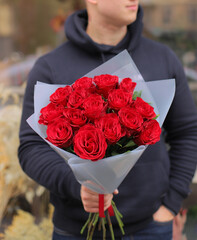Young man with a gift bouquet of red roses, mono bouquet of roses. Young man holding fresh bouquet of roses.
