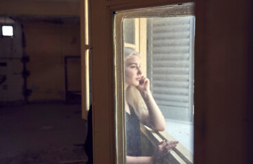 Close up portrait of beautiful blond young woman looking through hotel window