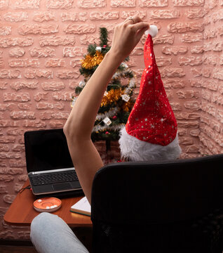 The girl is sitting back in a chair, holding a bubon of a new year's cap.