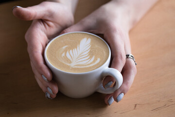 Top view of hot cappuccino coffee in the cafe, Heart shape cream coffee in blue cup. Hands women holding hot coffee in cup Asian woman smelling and drinking hot coffee with feeling good in coffee shop