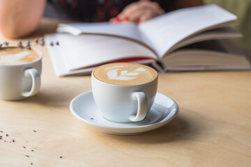 Top view of hot cappuccino coffee in the cafe, Heart shape cream coffee in blue cup. Hands women holding hot coffee in cup Asian woman smelling and drinking hot coffee with feeling good in coffee shop