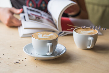 Top view of hot cappuccino coffee in the cafe, Heart shape cream coffee in blue cup. Hands women holding hot coffee in cup Asian woman smelling and drinking hot coffee with feeling good in coffee shop