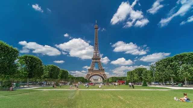 Eiffel Tower on Champs de Mars in Paris timelapse hyperlapse, France. Blue cloudy sky at summer day with green lawn and people walking around