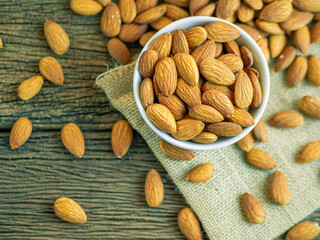 Almonds in white bowl on old wooden background.