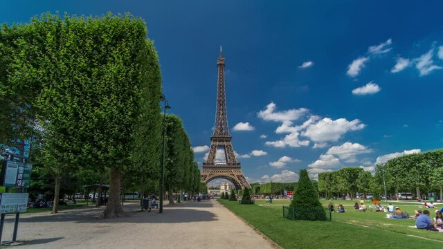 Eiffel Tower on Champs de Mars in Paris timelapse hyperlapse, France. Blue cloudy sky at summer day with green lawn and people walking around
