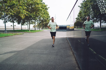 Motivated male jogger dressed in active wear running during morning time enjoying sportive...