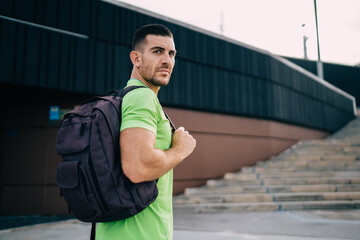 Half length of male bodybuilder with sportive backpack for gym stuff looking at camera during...