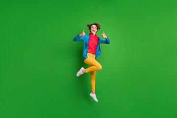 Full length body size photo of cheerful girl jumping high showing like thumb-up gesture isolated on vivid green color background