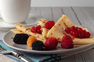 Thin pancakes with honey, raspberries, mulberries and currants