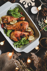 Winter festive food concept. Top view of dark vintage background, garland and candles. Christmas and New Year background. Baked chicken legs and potatoes.