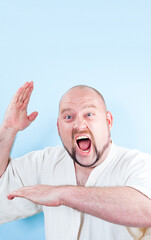 Studio photo of a funny man in a white robe making karate moves on a light blue background.