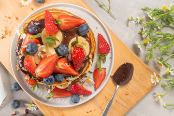 Fototapeta na wymiar Pancakes with chocolate paste and hazelnuts, banana, strawberry and blueberry