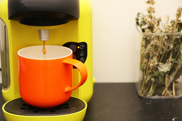 Coffee in a bright orange сup on the table. Close-up is a light green coffee maker with an orange cup.