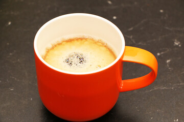 Coffee in a bright orange сup on the table. Close-up is a light green coffee maker with an orange cup.