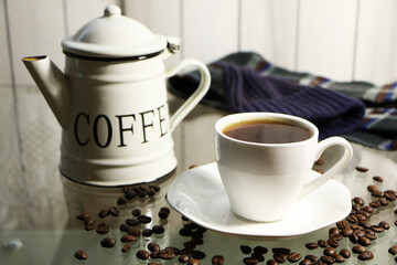 Cup of coffee and coffee beans on a glass table. The concept of home comfort and warmth.