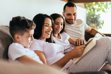 Latin family enjoying the day together at home. Family reading together on the couch in the morning.