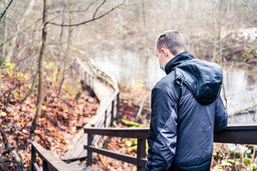 Man wearing a corona virus mask while walking outdoors in the nature in winter or autumn. Young person hiking the forest during coronavirus pandemic and quarantine. Happy hiker with facemask.