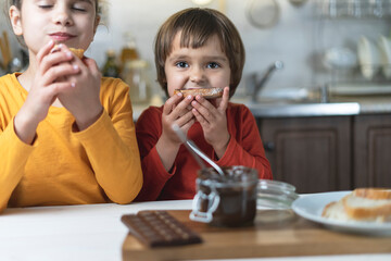 Sister and brother alone in the kitchen have breakfast on their own chocolate paste, smeared on the...