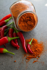 Red chili peppers and paprika powder in glass spice jar on stone table. Dark grey background with copy space. Ingredients top view photo. Vegetable texture close up. 

