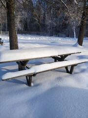 The bench and table are covered with snow. Winter landscape. New Year's time. There is a lot of snow outside. Forest zone. Soft, white, fluffy snow. Background for the screen.